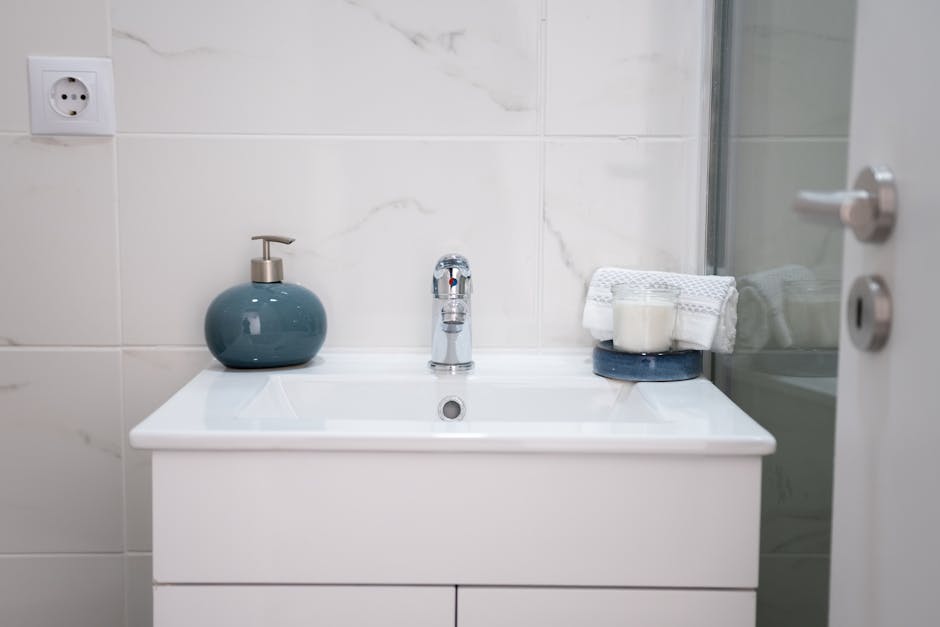 A clean, modern bathroom setup with a white sink, chrome faucet, soap dispenser, and towels.